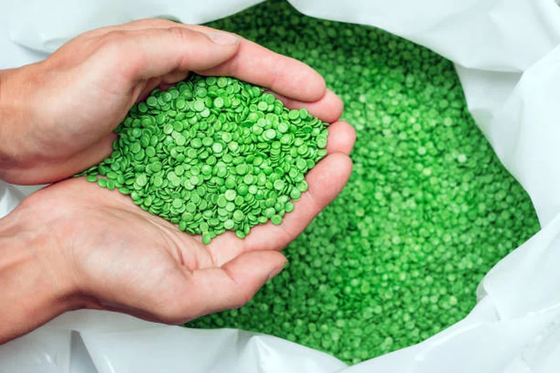 Green recycled PE pellets held in hands inside a bag